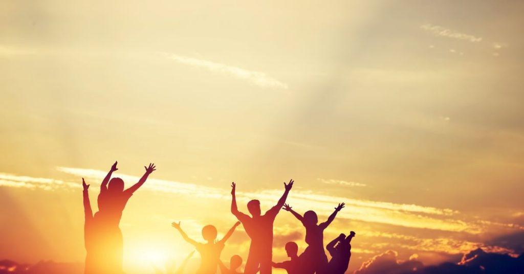The Power of Self Worth A group of people dance in the sunrise shown as silhouettes against the light background